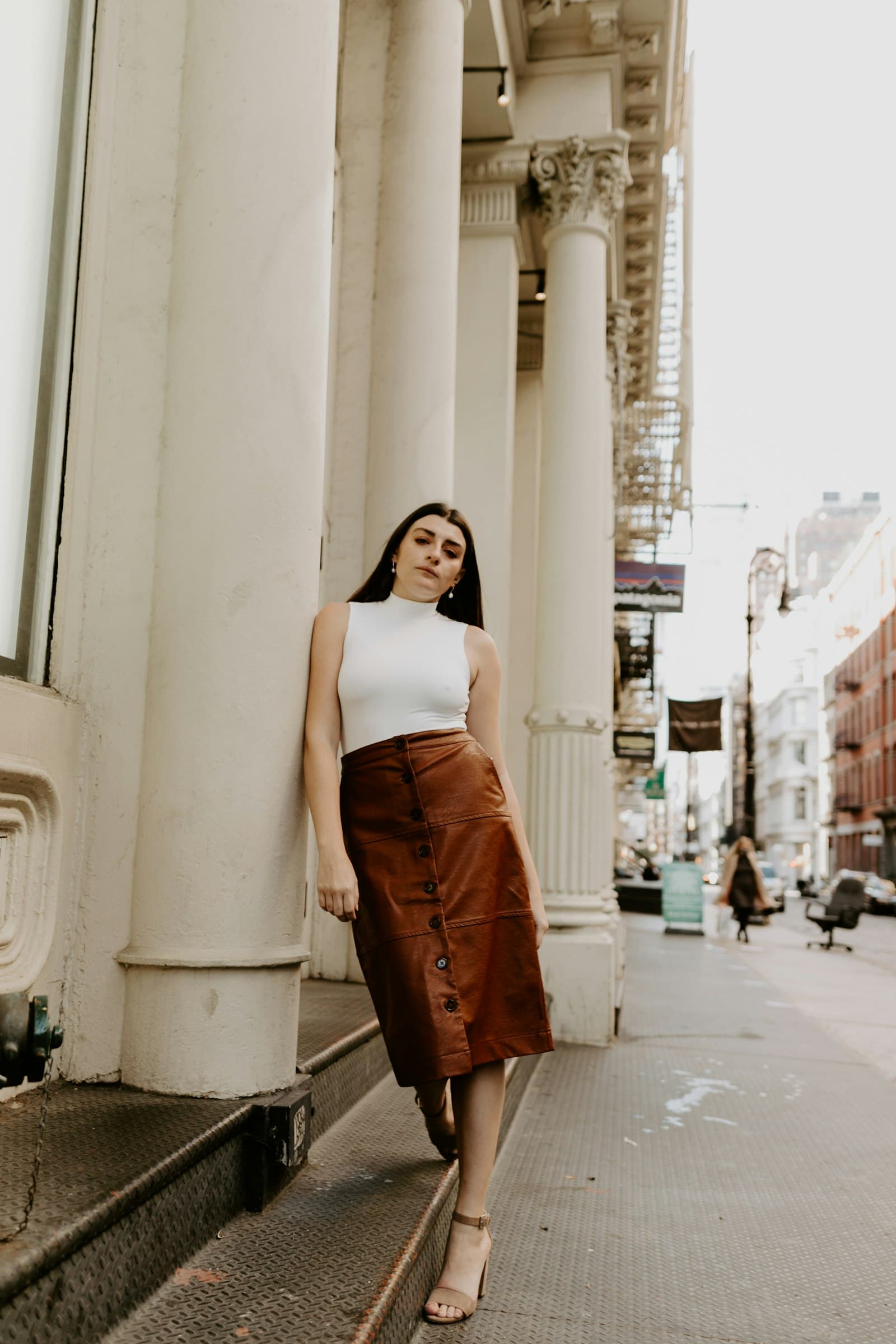 Woman in white tank top and brown skirt standing on sidewalk during daytime