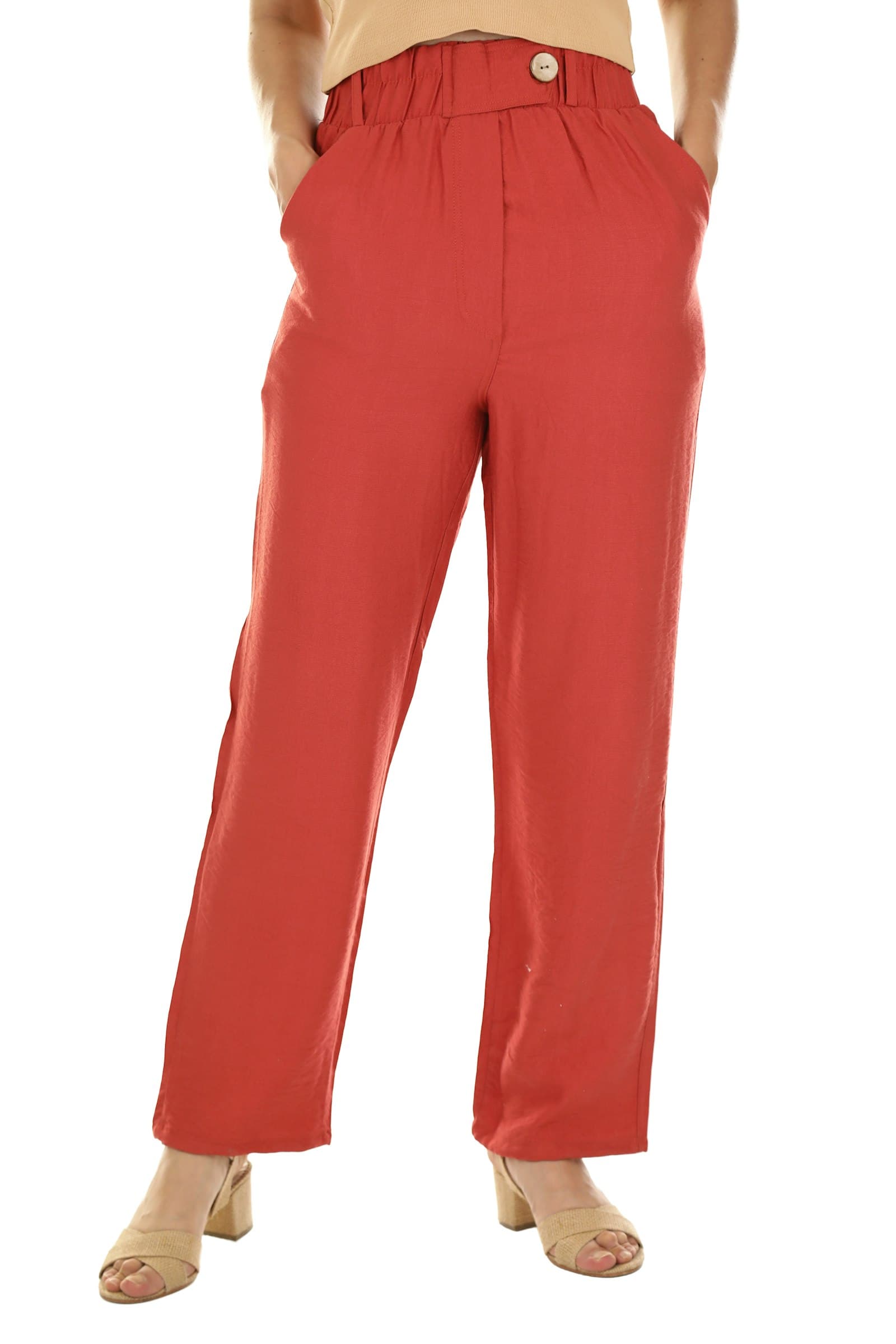 A person wearing red linen trousers and a beige top with tan sandals